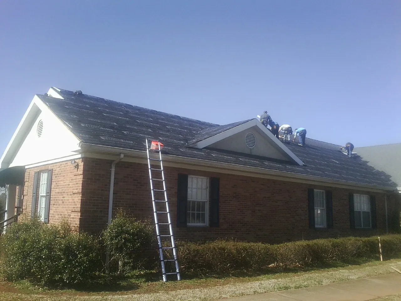 Crew tearing shingles off a brick ranch roof with a ladder set — Metal Roof Repair work by our crew in Vicksburg