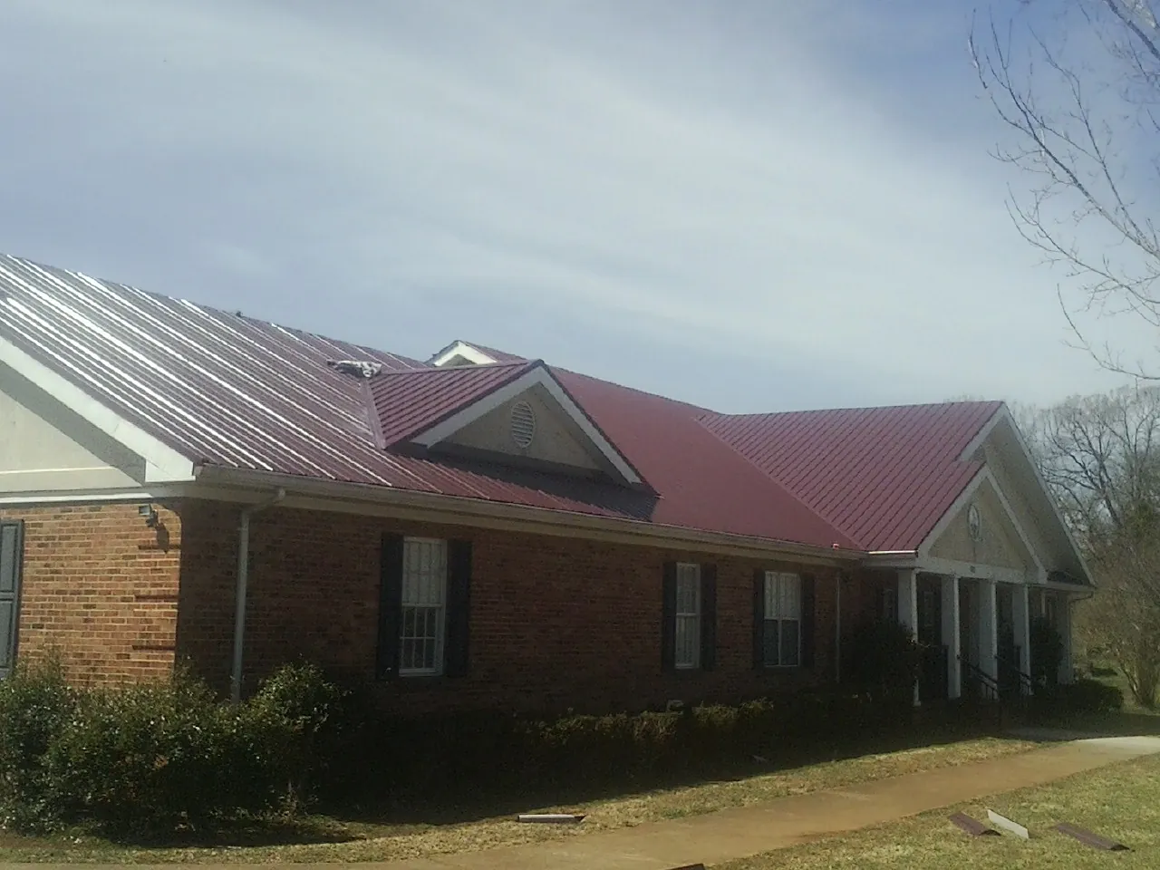 Red metal roof with gabled entries on a long brick building, from a Hail Damage Roof Repair job in Vicksburg