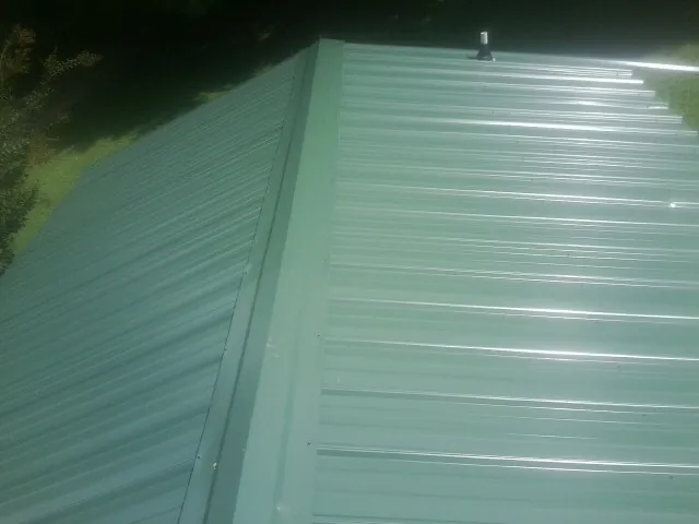 New green metal panels meeting at the ridge of a roof — Flat Roof Repair work by our crew in Vicksburg