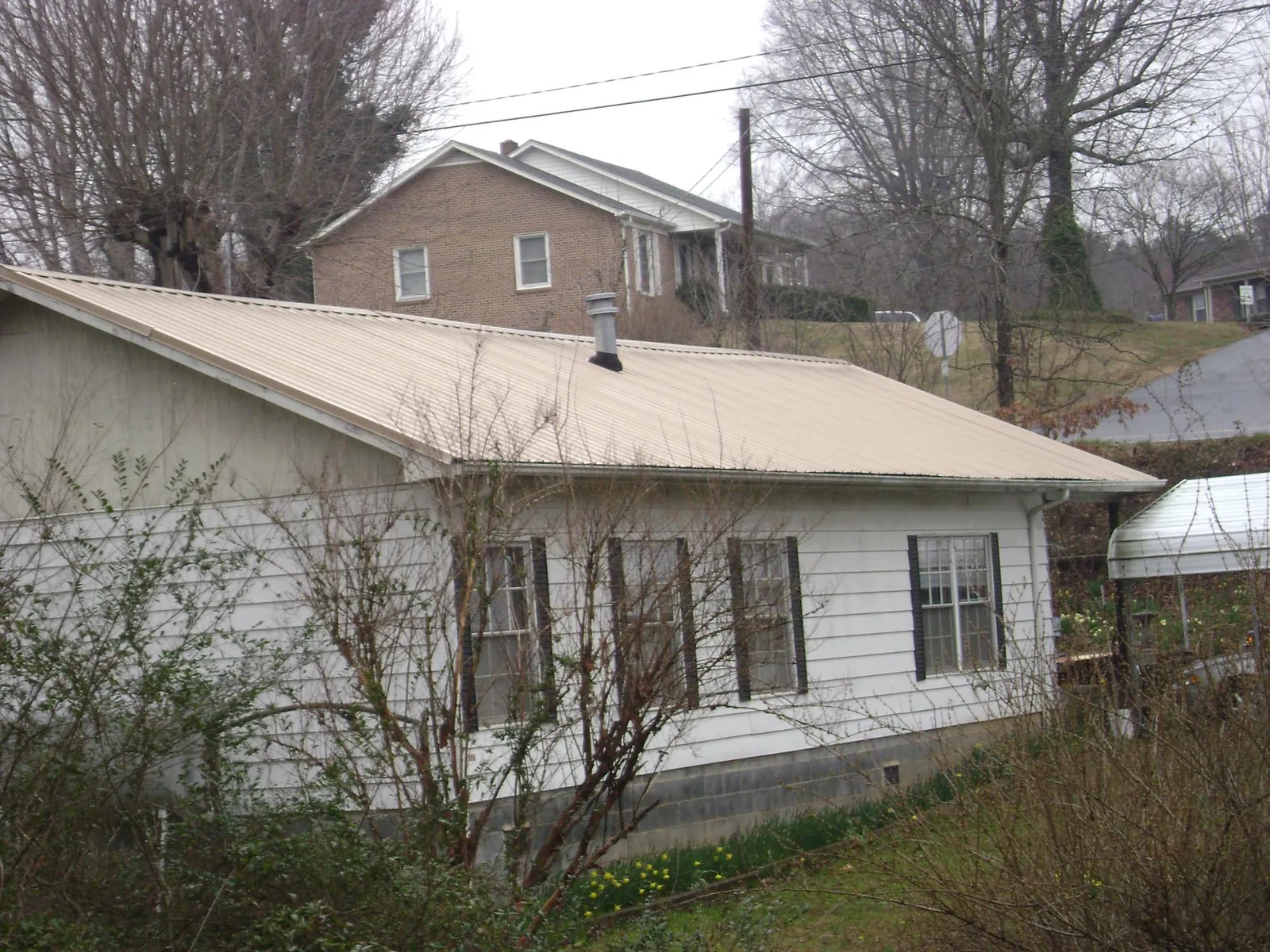 Tan metal roof on a white sided house set into a hillside — Commercial Roofing by Roofing Brothers in Vicksburg
